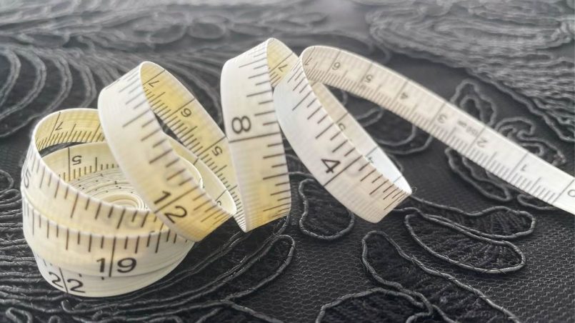 A woman using a fabric tape measure to check her bust circumference for a vintage dress