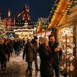 Visitors browsing handcrafted ornament stalls at the Bethlehem Christkindlmarkt at night with festive lights in the background