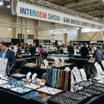 Colorful gemstones and jewelry displayed on tables at the San Mateo County Event Center during the InterGem show