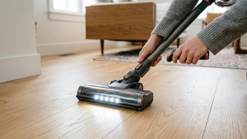 Modern self-standing cordless vacuum upright on a hardwood living room floor.